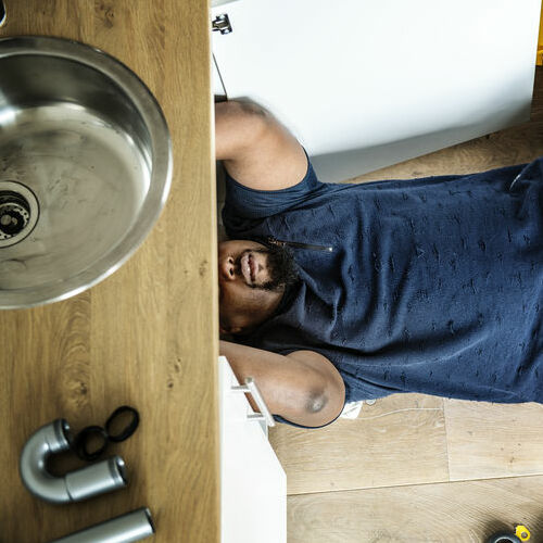 A Plumber Works under a Sink