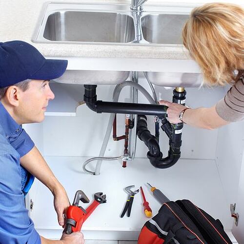 A Plumber Inspects Pipes Under a Sink.